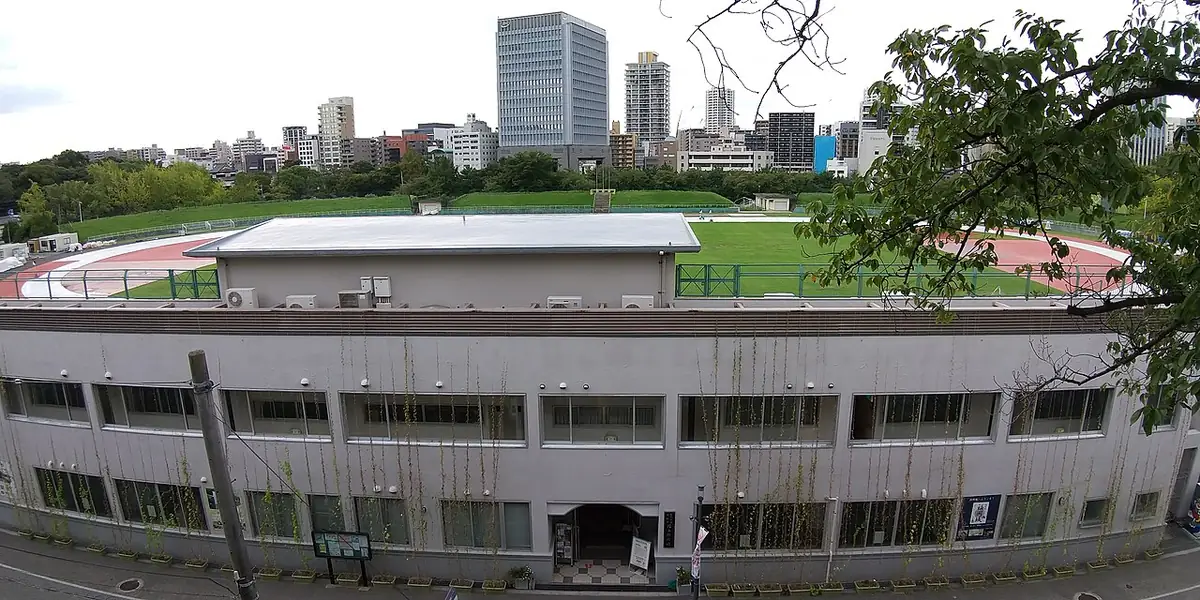 平和台陸上競技場の建物とトラック、後ろに福岡市のビルが見える写真